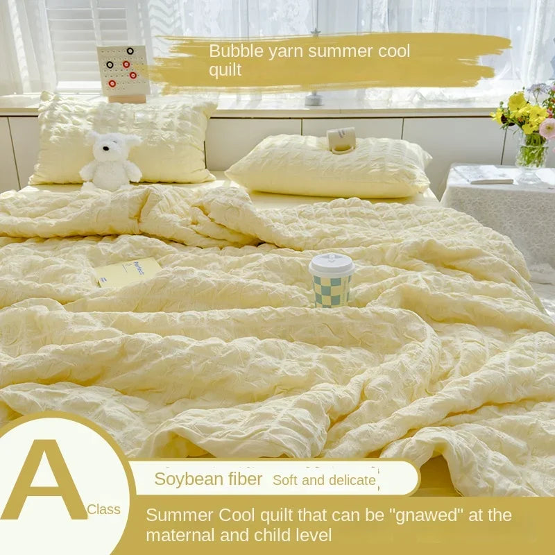 A yellow bubble yarn summer cool quilt displayed on a bed with white pillows and a white table.