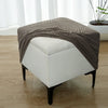 A beige geometric jacquard stretch ottoman cover draped over a white upholstered ottoman.