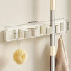 A white wall-mounted holder for a mop and broom with detachable hooks, featuring measurement markings.