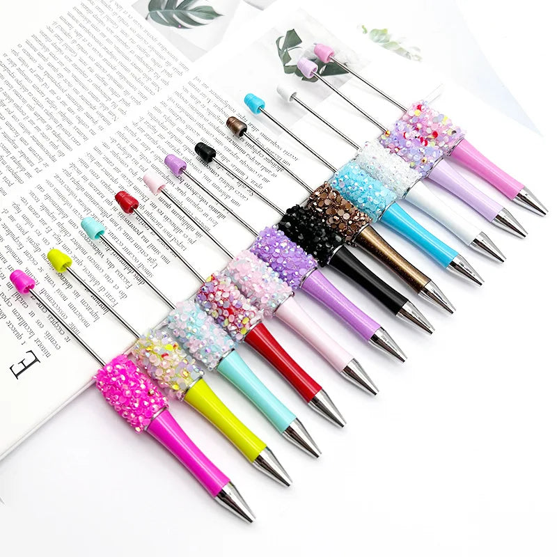 A collection of twelve ballpoint pens featuring various glitter and sequin designs in pink, purple, blue, and gold.