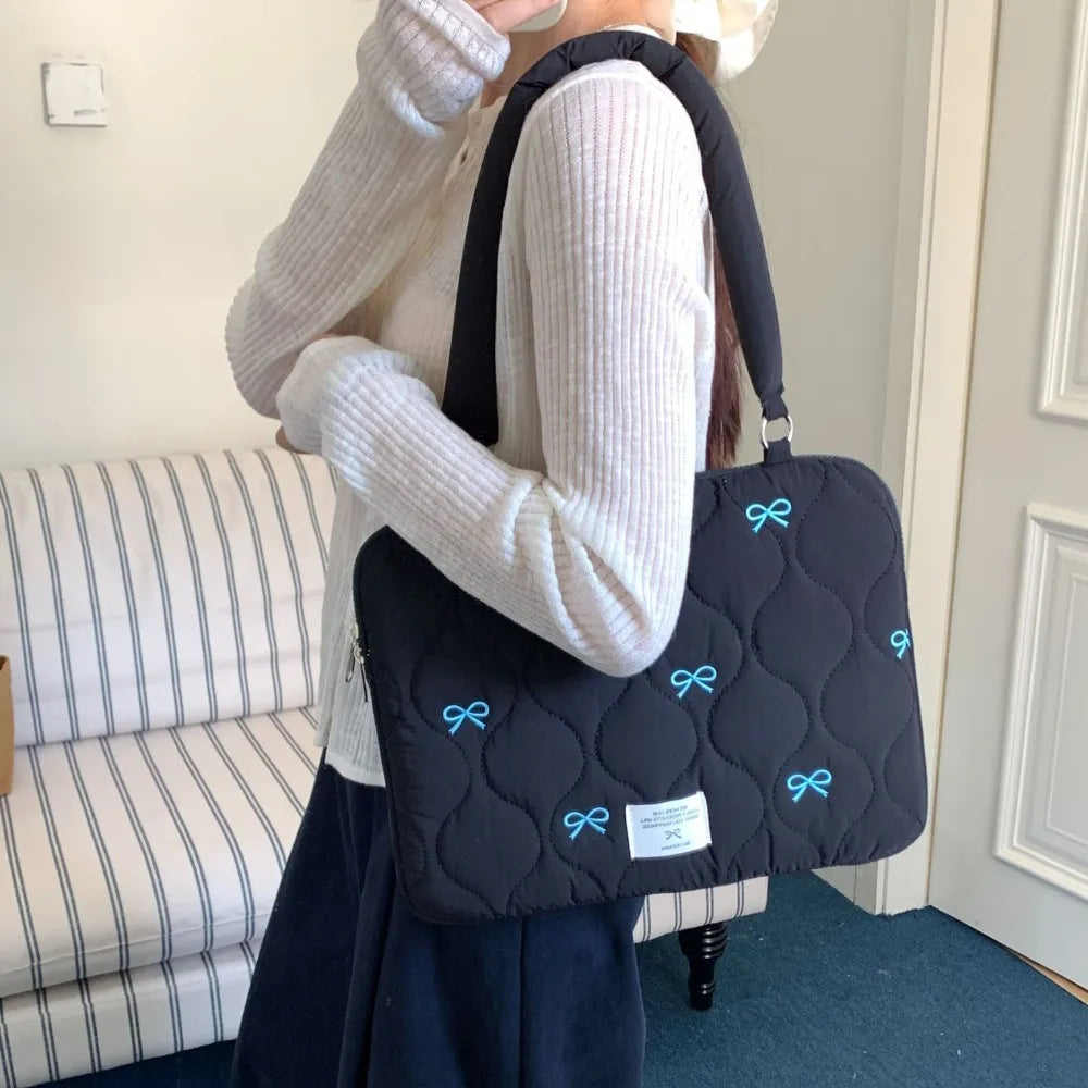 A person is holding a black quilted laptop shoulder bag with blue bows and padded protection.