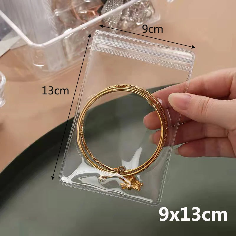 A hand holds a clear plastic pouch containing a gold-colored ring, demonstrating the size of the jewelry storage.