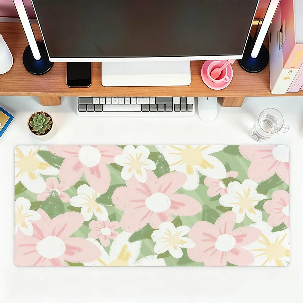 A pink and green floral mouse pad with white and yellow flowers placed on a wooden desk next to a computer setup.