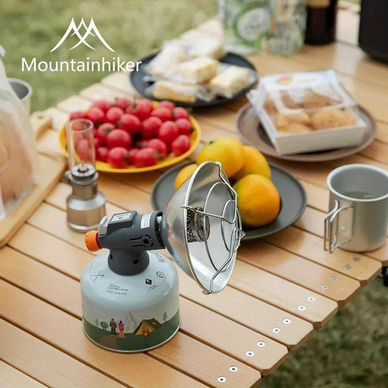 A portable butane gas stove is set up outdoors on a wooden table with food items like tomatoes and lemons.