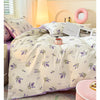 Helle lavendelfarbene Blumendecke auf einem Bett mit weißen Laken und einem rosa Akzentkissen.