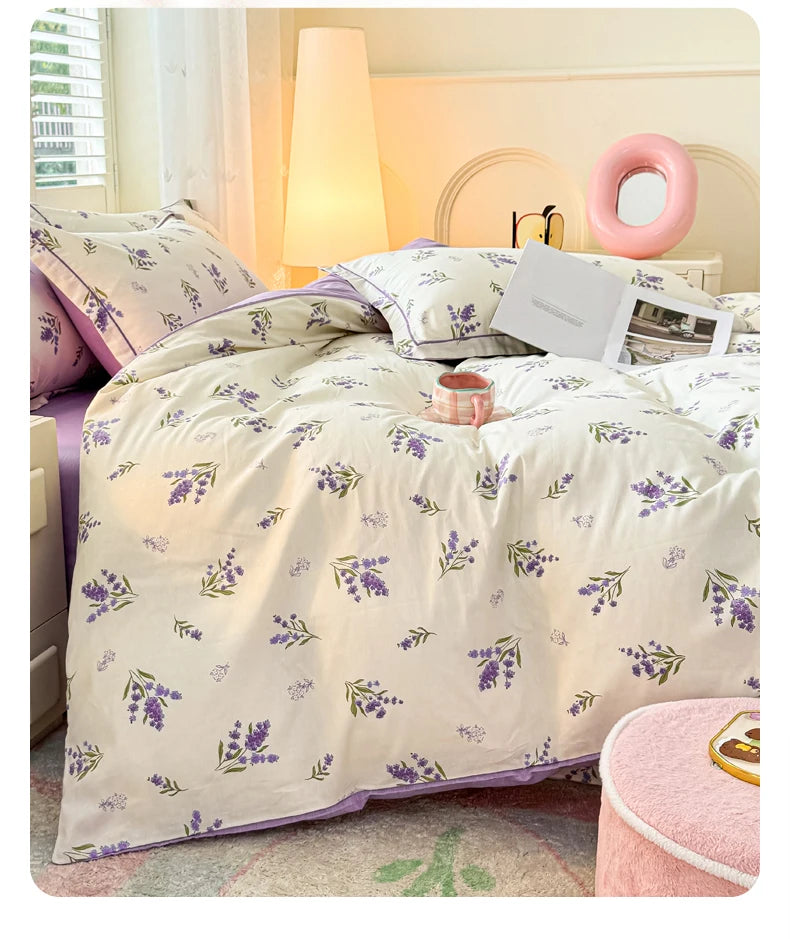 Helle lavendelfarbene Blumendecke auf einem Bett mit weißen Laken und einem rosa Akzentkissen.