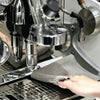 A hand is placing a gray waffle weave microfiber kitchen towel onto a metal grid in a waffle maker.