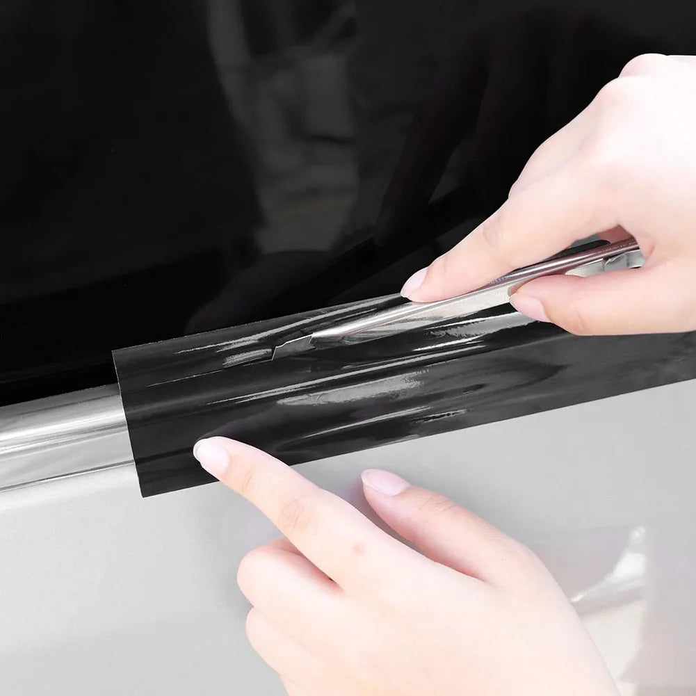 A hand is applying a high-gloss black vinyl wrap strip to a car surface.