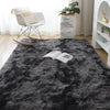 A dark gray Nordic furry accent rug placed on a wooden floor with a white chair and potted plant in the background.