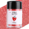 A glass jar of red edible glitter powder labeled Red with a strawberry illustration, set against a red glitter background.