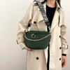 A woman holds a dark green quilted woven pattern waist bag with a black and white patterned strap against a light beige trenc