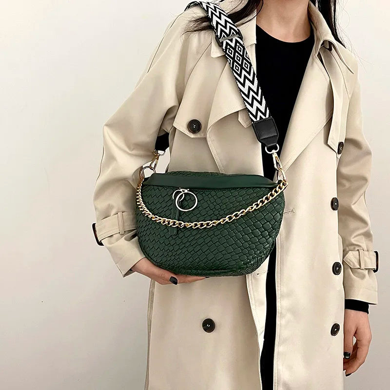 A woman holds a dark green quilted woven pattern waist bag with a black and white patterned strap against a light beige trenc
