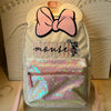 A light cream backpack featuring a pink bow and a front pocket filled with sparkly pink and green fabric.