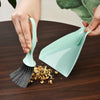 A hand is using a compact mini broom and dustpan set to clean a dark wooden surface.