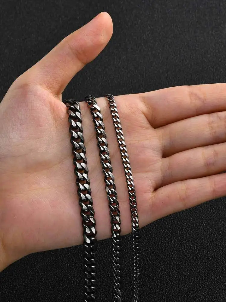 A hand holds several stainless steel Cuban link chains of varying lengths against a dark background.