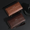 Portefeuille pochette en cuir marron avec fermeture éclair et sangle sur une surface sombre.