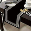 Black geometric table runner and placemat set with gold accents and a gray napkin roll.