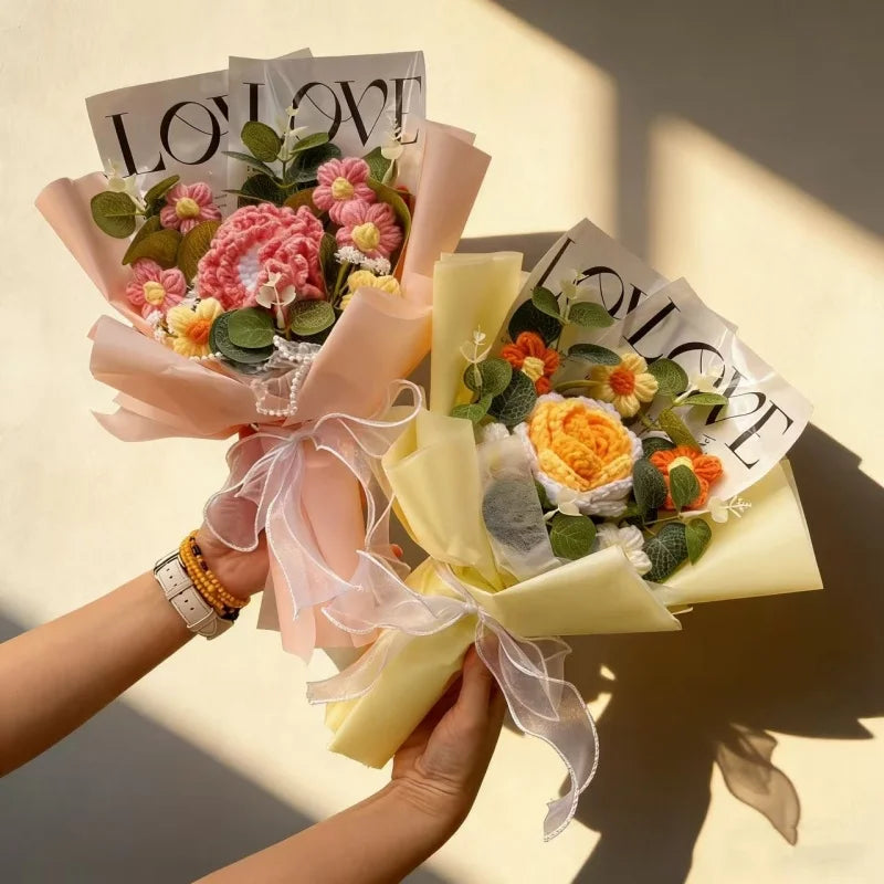 A hand holds a bouquet of handmade crochet artificial flowers wrapped in pink and cream paper.