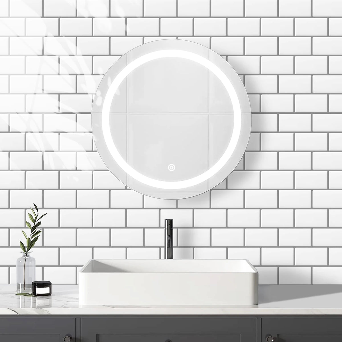 A modern bathroom featuring a white vessel sink and a round illuminated mirror mounted on a white subway tile wall.