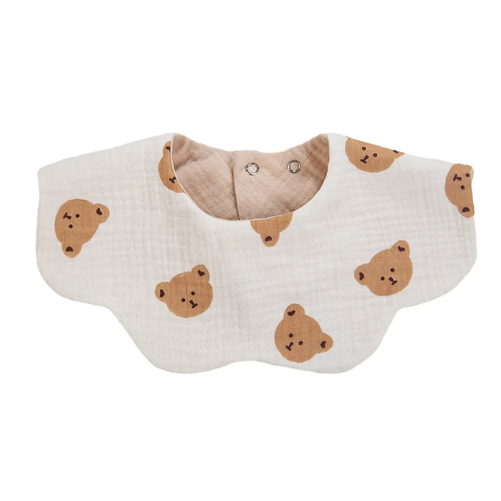 A light beige muslin cotton baby bib with a bear pattern and adjustable snap closure.