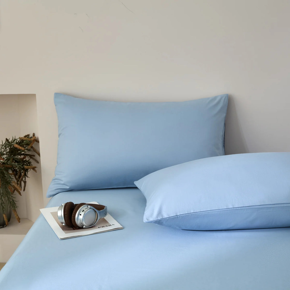 Light blue quilted duvet cover set with matching pillowcases and a pair of silver headphones on the bed