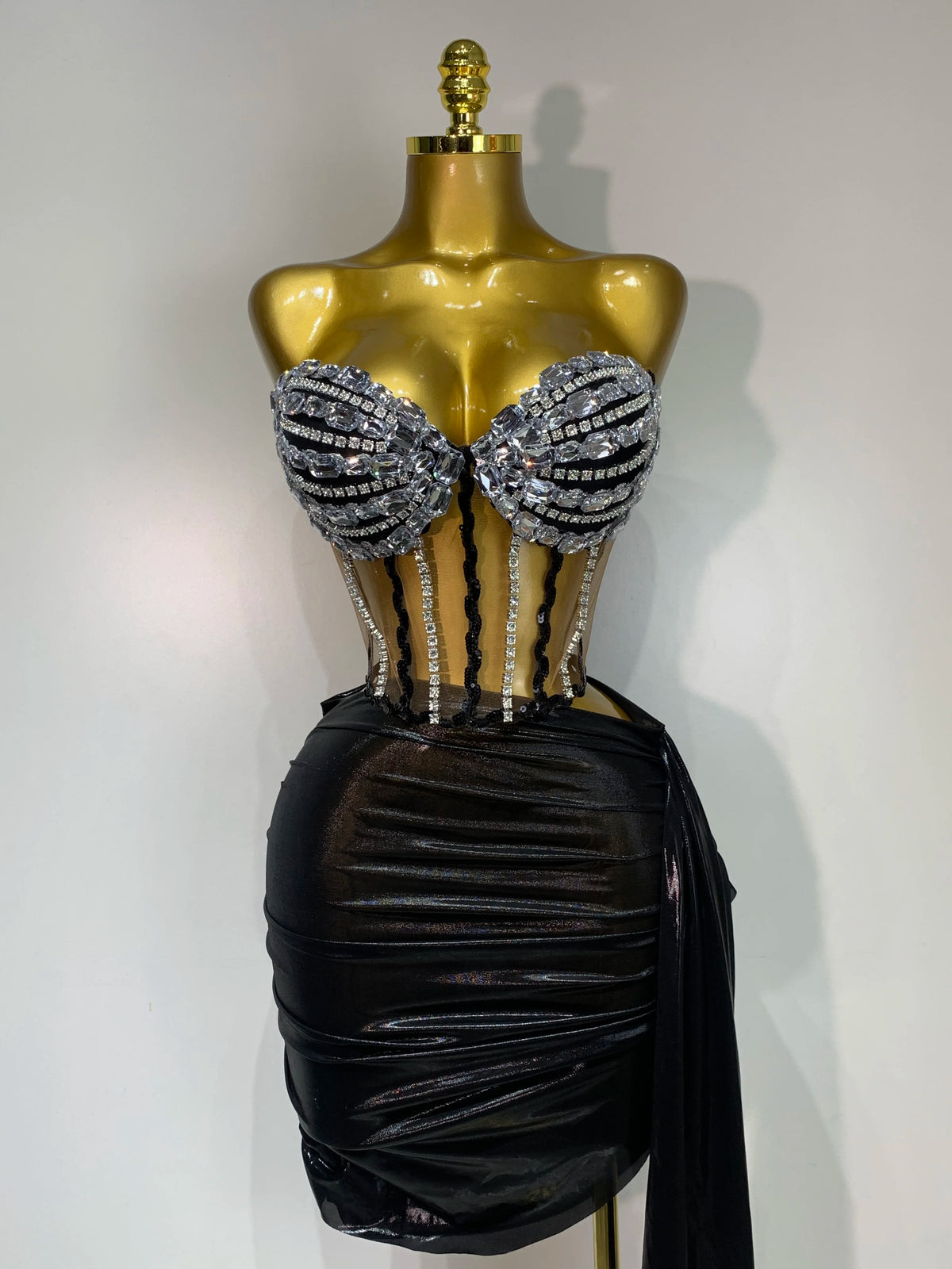 A gold mannequin displays a sparkly two-piece party outfit with a sheer top and a black draped skirt.