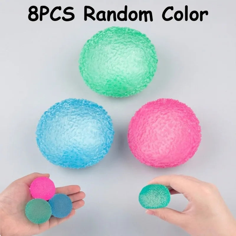 Eight colorful, soft textured stress balls in various shades are displayed on a gray surface and held by hands.