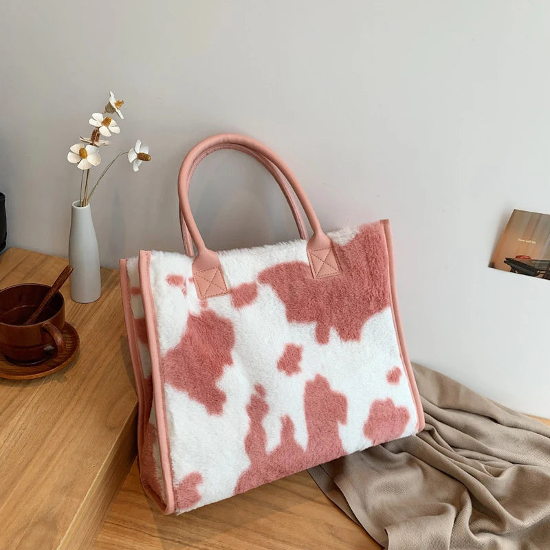 A pink faux fur tote bag with a white leopard print and pink trim resting on a wooden surface.