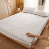 A hand is touching a white quilted mattress protector with extra padding on a bed.