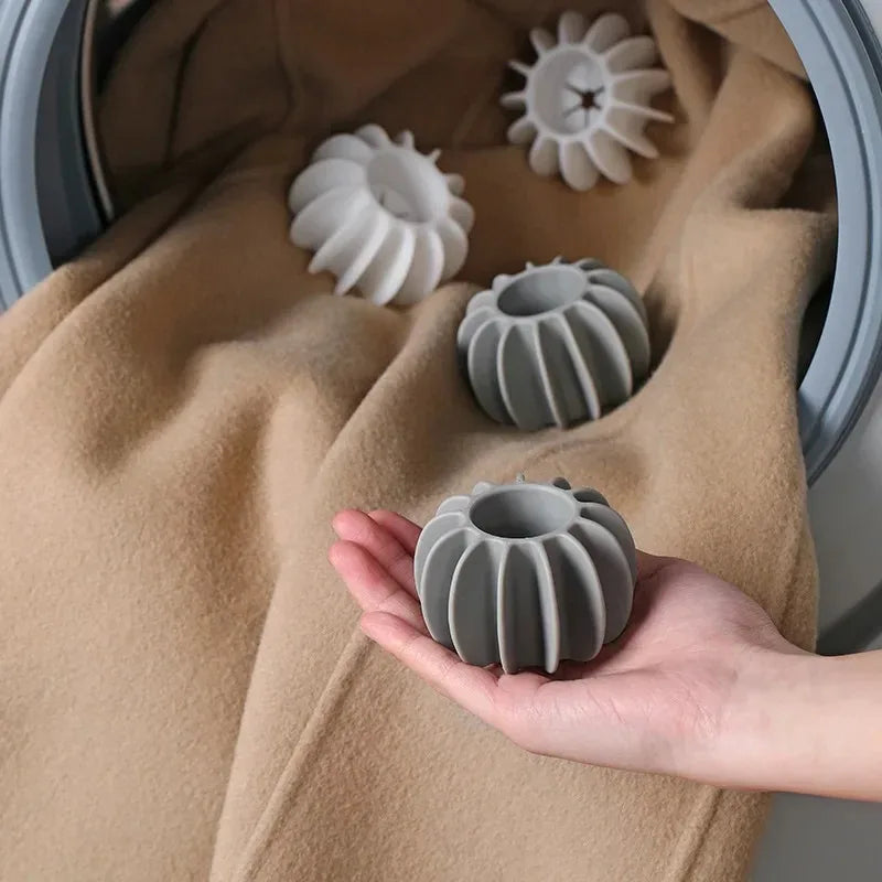 A hand holds a grey reusable laundry ball for pet hair and lint removal against a tan fabric background.