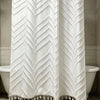 White shower curtain with a geometric cutout tassel pattern hanging on a rod.
