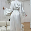 A woman wearing a long white silk satin robe with lace trim, shown from the back.