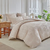 A beige duvet cover set with a subtle leaf print pattern displayed on a bed in a bright room.