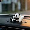 A white and black panda figurine is placed on a dark surface, likely in a car or on a desk.