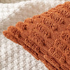 A close-up of a rust orange corduroy throw pillow cover with vertical ribbed texture resting on a light beige fabric.