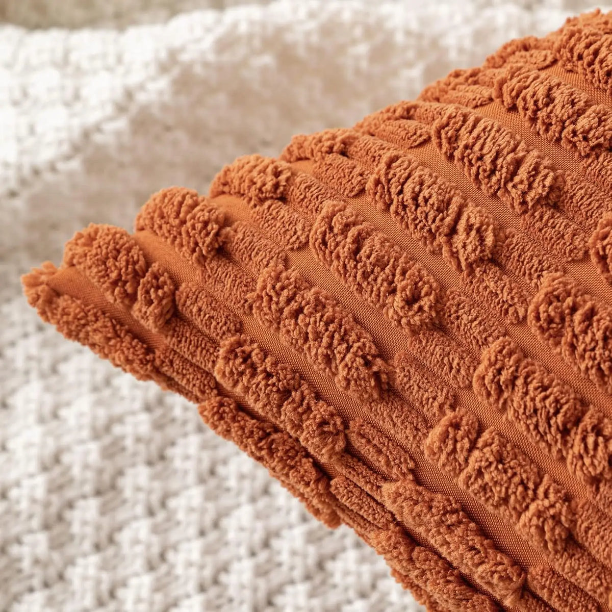 A close-up of a rust orange corduroy throw pillow cover with vertical ribbed texture resting on a light beige fabric.
