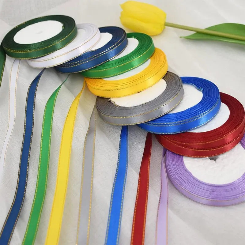 A collection of gold-edge satin ribbons in various colors including green, white, blue, yellow, and red, laid out on a white 