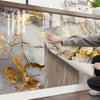 A hand is touching a marble surface featuring gold veining and gray tones on a kitchen backsplash.