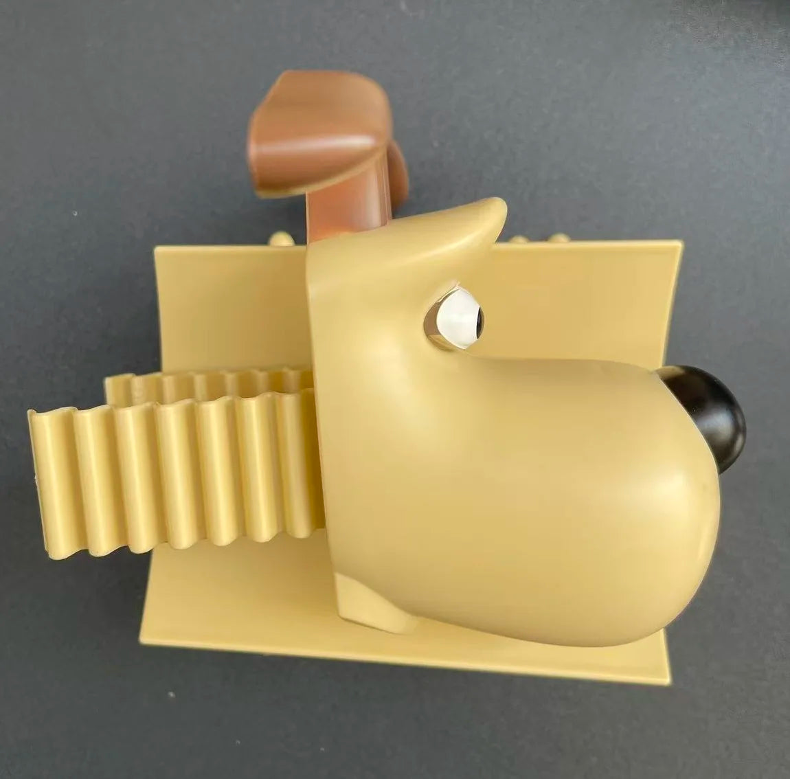 A beige plastic animal shaped toilet paper holder with a brown head and ribbed body.