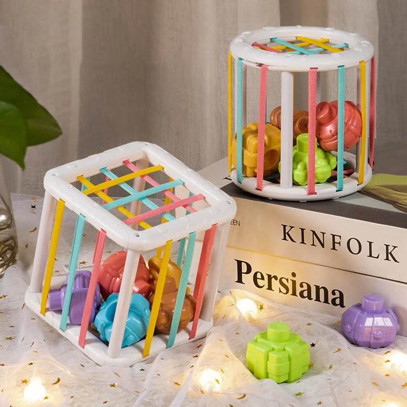 A white rainbow shape sorter cube with colorful elastic bands is shown next to a stack of books.