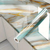 A roll of teal and gold marble contact paper displayed on a glass surface.