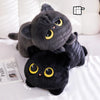 A soft black cat plush toy with yellow eyes is resting on a white surface.