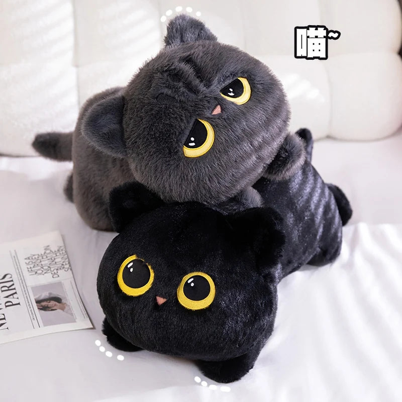A soft black cat plush toy with yellow eyes is resting on a white surface.