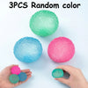 Three random colored soft textured stress balls are shown on a white surface with hands holding some of them.