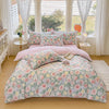 A floral printed duvet cover set in soft pink and green tones displayed on a bed with white curtains.