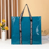 A teal shopping bag with black handles is displayed against a beige background.