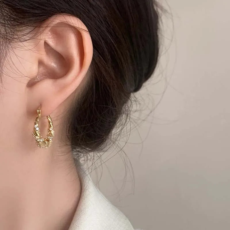 Gold twisted zircon hoop earrings worn on a person's ear.