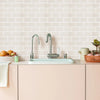 A kitchen sink setup with a chrome faucet and white countertop against a light pink tiled wall.
