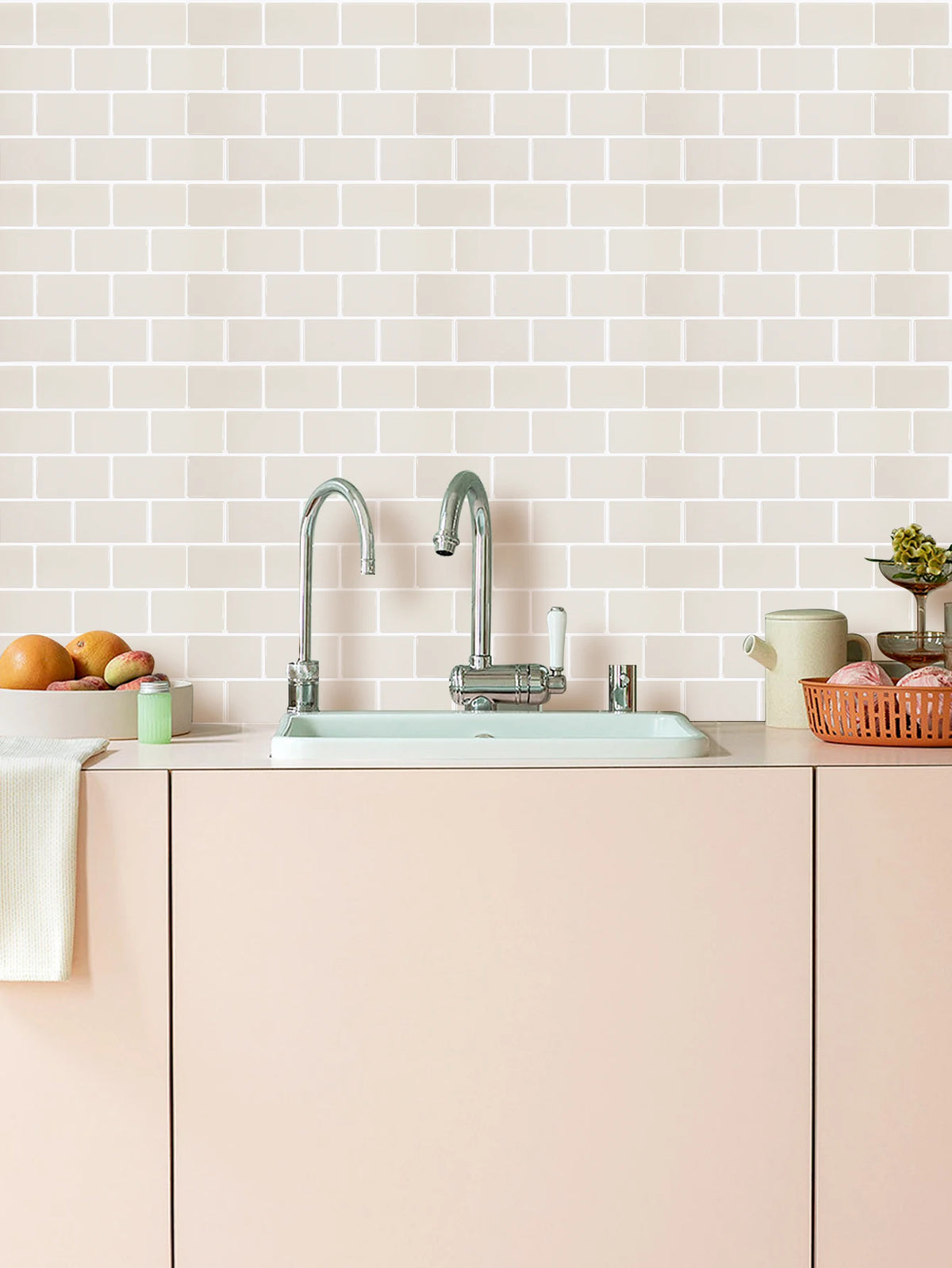 A kitchen sink setup with a chrome faucet and white countertop against a light pink tiled wall.