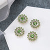 A collection of five green and clear rhinestone flowers on a white surface.